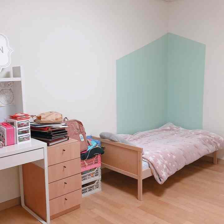 A cozy kids' room featuring a blue-green mint corner wall, wooden bed, and desk