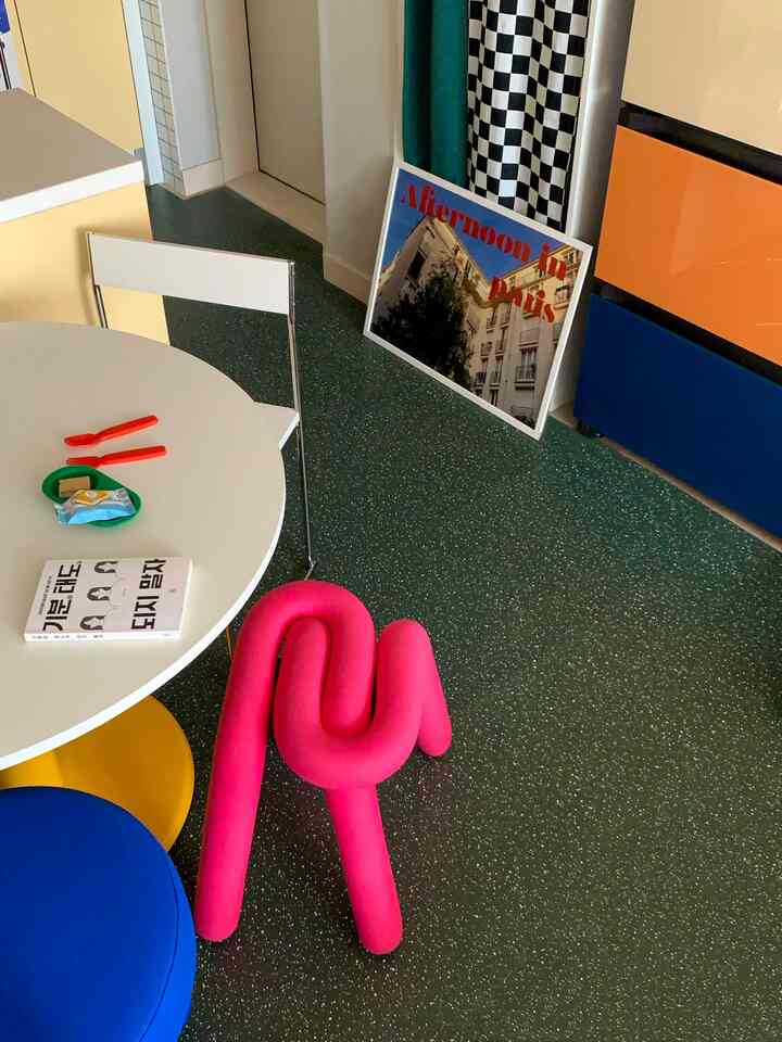 白と青のトーンのモダンなキッチンスペース、丸いダイニングテーブルとピンクのスツールが配置された印象的な空間