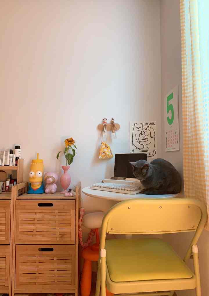 Yellow-toned compact space with round desk, cat, and decorative objets creating cozy workspace