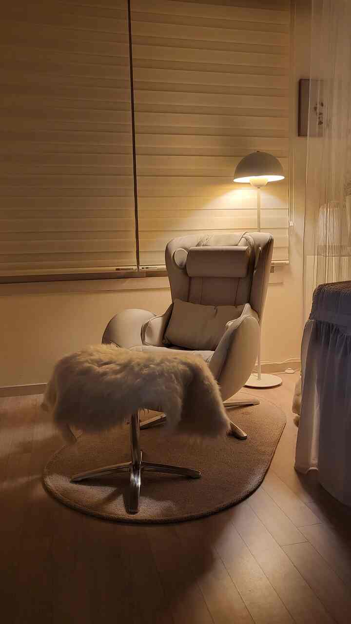 Warm beige-toned studio apartment featuring a massage recliner, floor lamp, and rug with cozy atmosphere