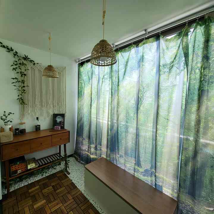 Natural toned small space featuring wooden furniture, rattan lighting, plants, and forest-patterned curtains