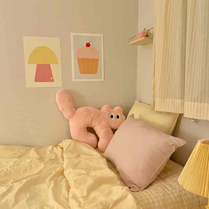 黄色とピンクのクッションと寝具が置かれた寝室、かわいいキャラクターポスターと柔らかな照明で雰囲気のあるインテリア