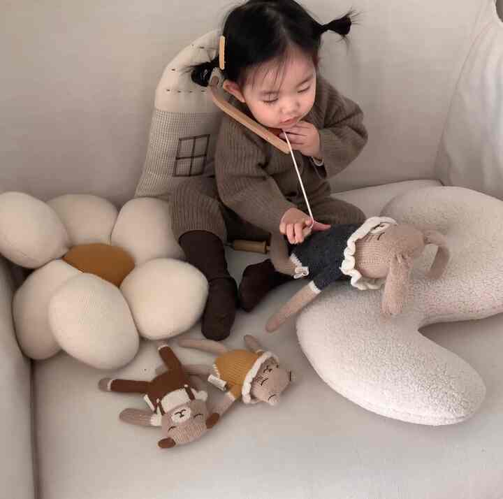 Beige and white toned kids' room featuring a toddler engaged in role play with large cushions creating a cozy atmosphere