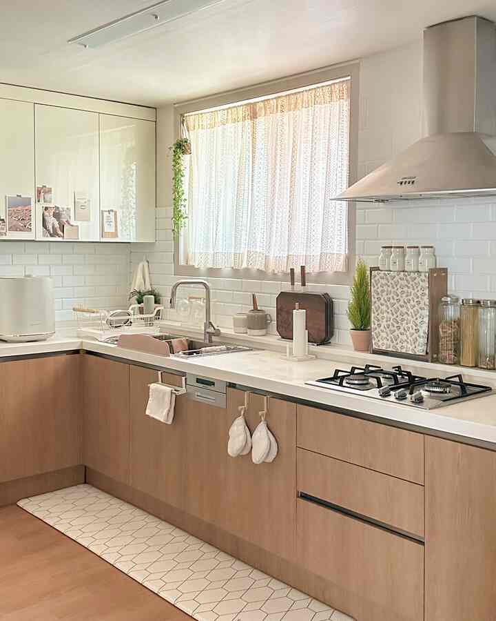 Natural style kitchen in white and wood tones, featuring a window with lace curtains, clean tiles, and visible storage organizers