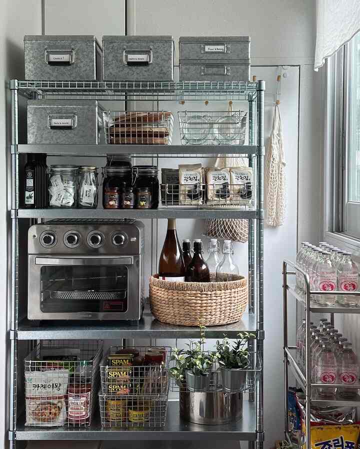 Silver and gray toned pantry space featuring stainless steel shelving, wire baskets, oven, and neatly organized kitchen storage items
