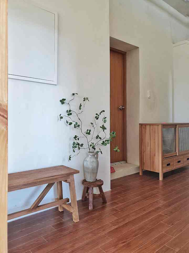 ナチュラルな木目調と白い壁が調和するリビング、ヴィンテージの花瓶とラフな古材スツールが配置された雰囲気のあるインテリア