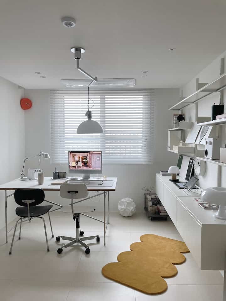 White-toned study featuring a white desk, office chairs, and a yellow rug in a simple home office setting