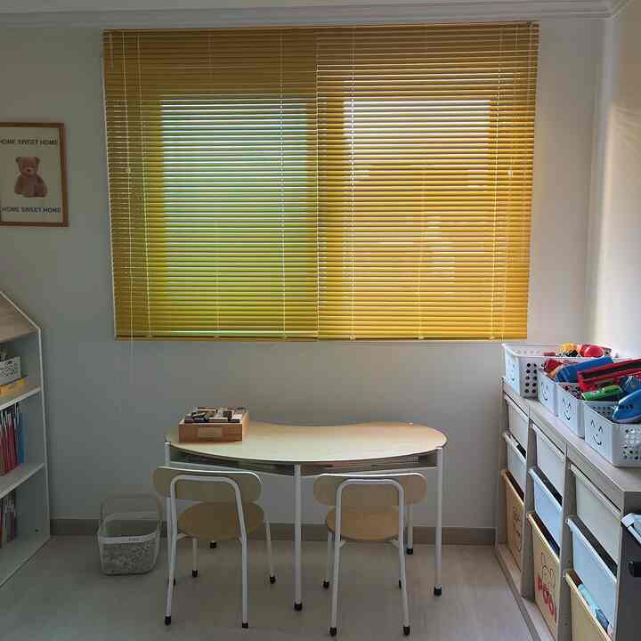 Cozy kids' room featuring warm yellow blinds, child-sized desk, and organized toy storage, creating a neat interior space