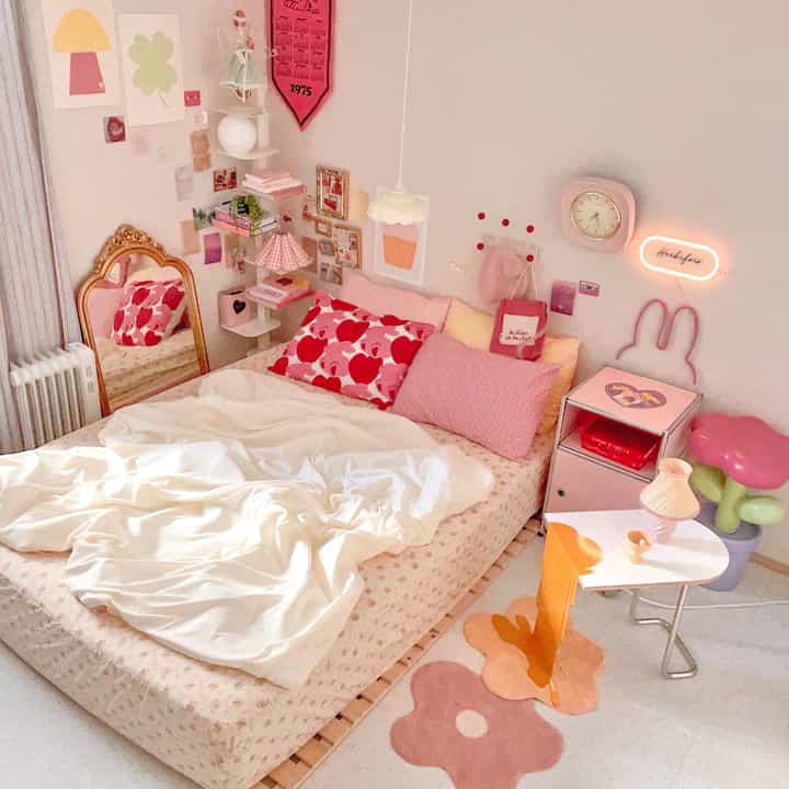 A pink and beige toned bedroom featuring floral bedding, a gold-framed standing mirror, and a cozy side table arrangement