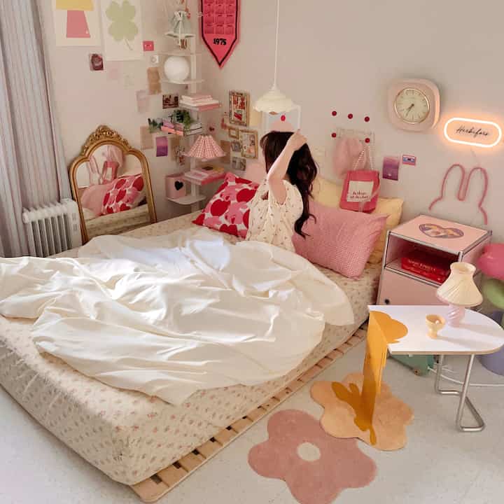 Cozy bedroom in pink and white tones featuring floral rugs, golden mirror, and unique wall decorations