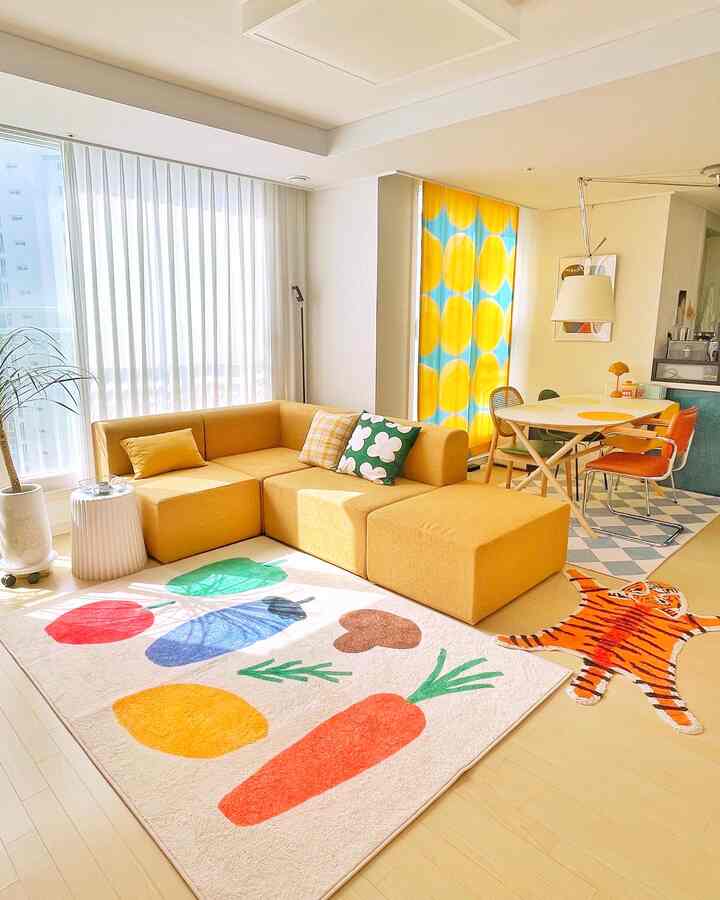 Bright yellow-toned living room featuring a yellow sofa, curtains, and a colorful vegetable print rug creating a cozy space