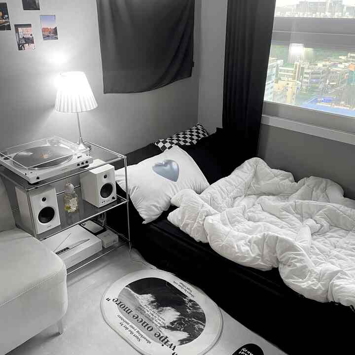 Monotone modern studio bedroom featuring a black bed with white bedding, turntable, and a simple lamp, creating a clean and minimal atmosphere