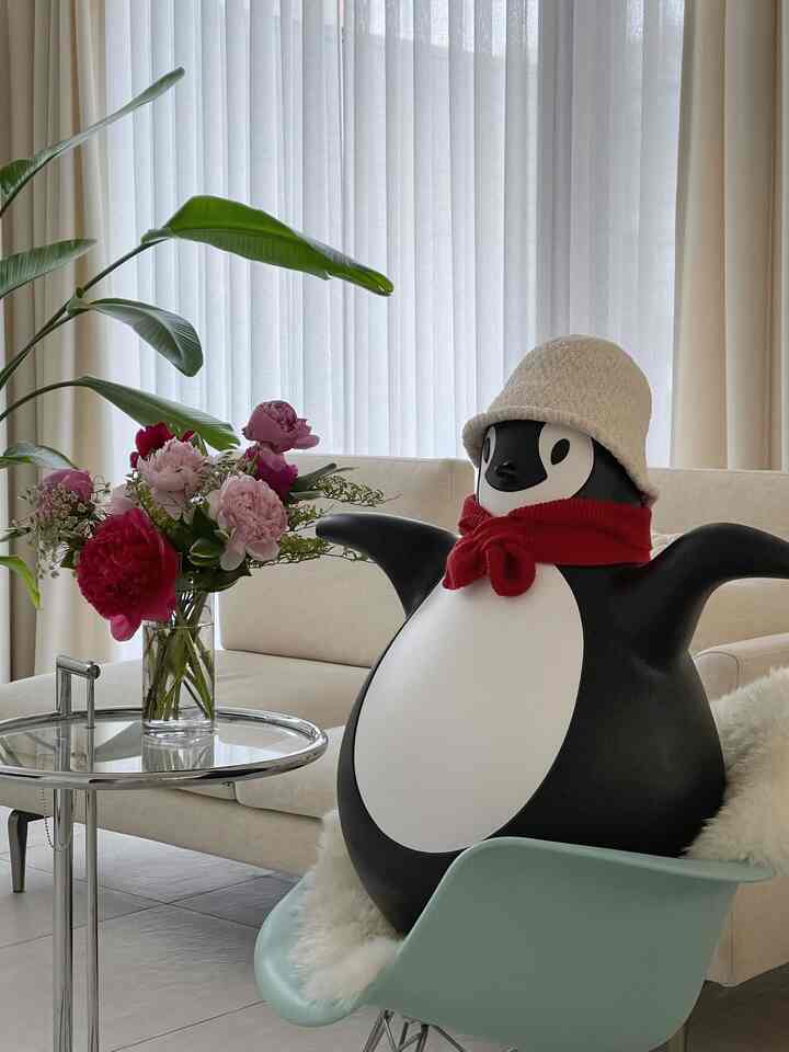 Natural ivory-toned living room featuring an Eames armchair holding a Magis Pingy penguin figure and a vase on a glass coffee table