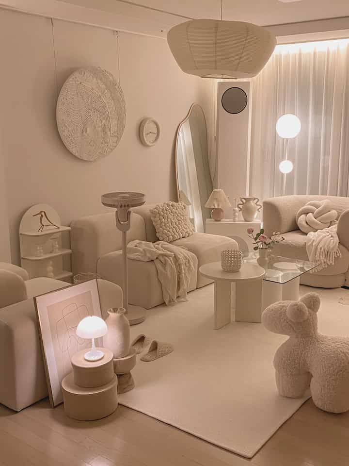Ivory and beige toned living room featuring modular sofa, round tables, and portable lamp creating cozy atmosphere