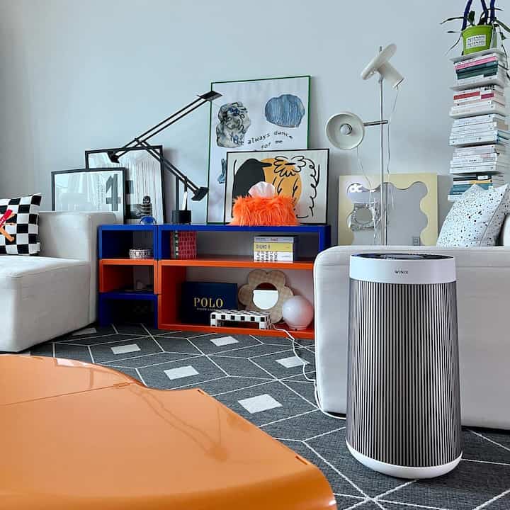 Modern living room in white and orange tones featuring an air purifier, colorful shelves, and a patterned rug