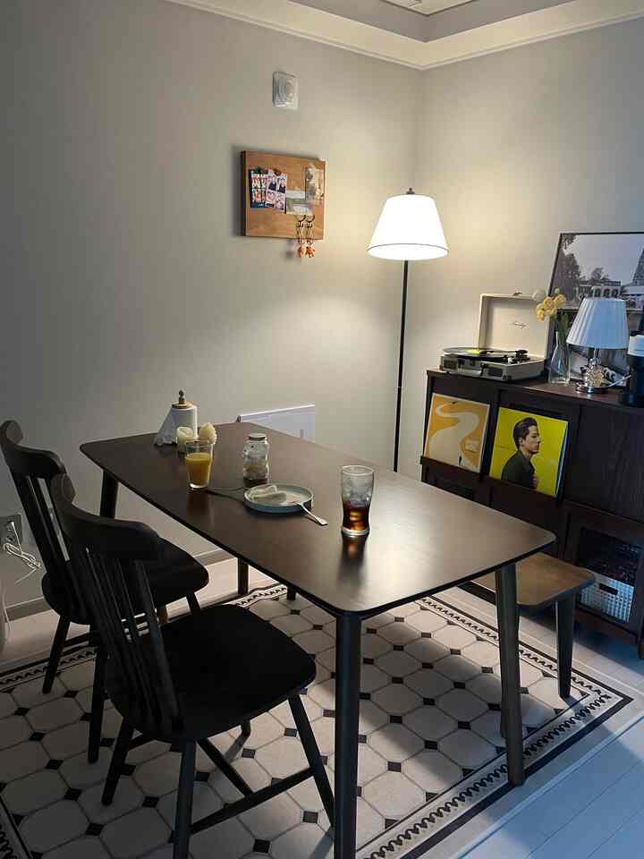 Brown wood-toned dining room for four people featuring natural wood dining table, chairs, floor lamp, and vintage cabinet with records
