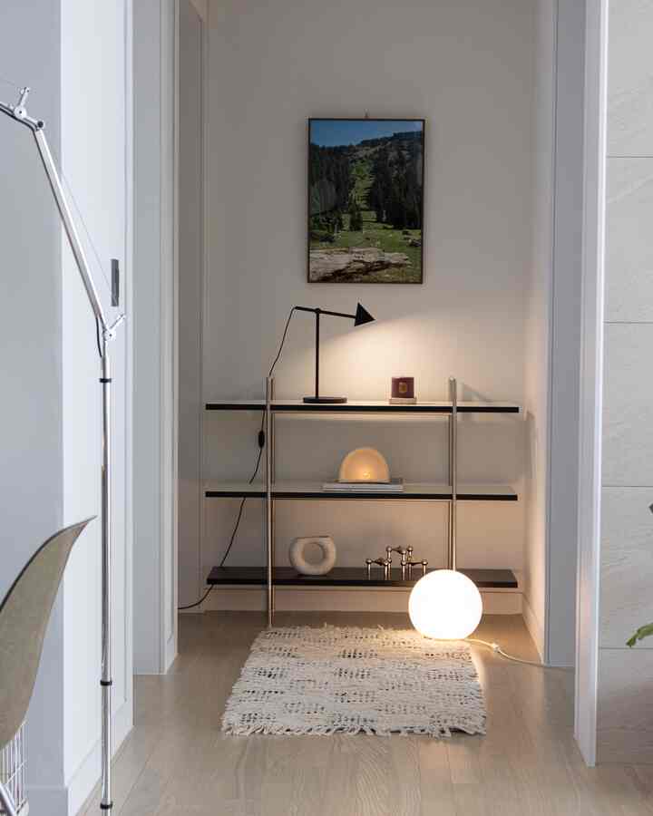 Natural toned living room corner with a minimalist bookshelf, rug, and various lighting elements creating a cozy atmosphere