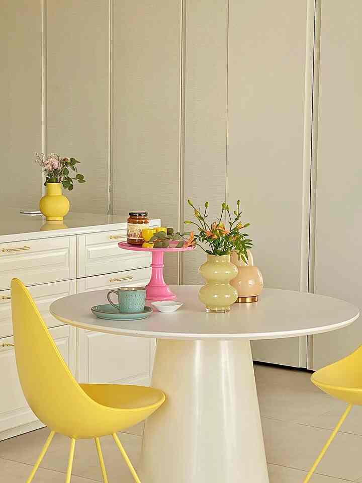 Pastel-toned dining room featuring a white round dining table and yellow dining chairs in a clean, cozy Nordic style space