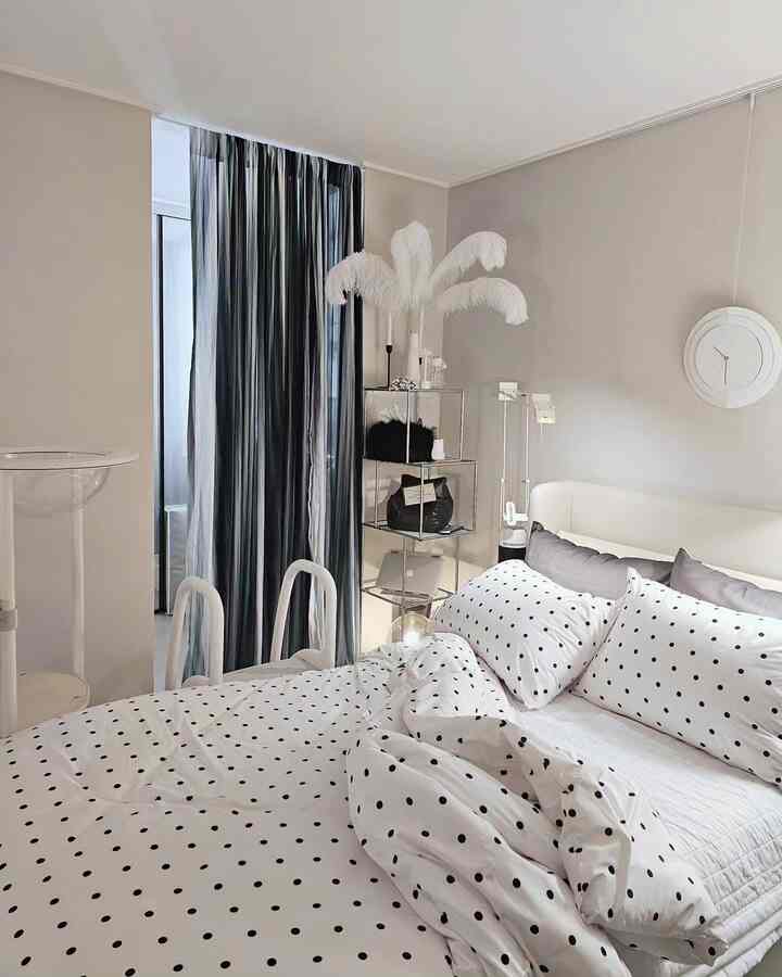 A modern bedroom in white and gray tones featuring polka dot bedding and sleek furniture with a clean, stylish atmosphere