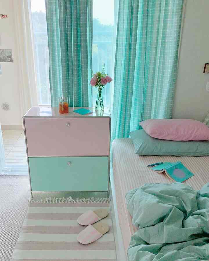 ミントとピンクの色調の4.5畳の寝室、窓際にカーテンと引き出しユニットが配置された落ち着いた雰囲気の空間