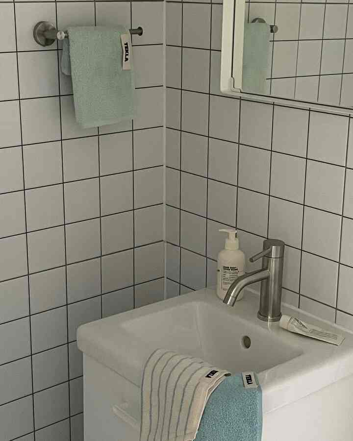 White tiled bathroom with a compact sink and mint towels, showcasing a small dry bathroom setup