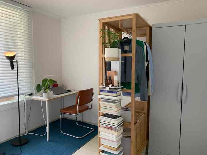 ナチュラルな色調のホームオフィス、窓際にデスクと椅子が配置され、木製の本棚に本と植物が整然と置かれた印象的な空間