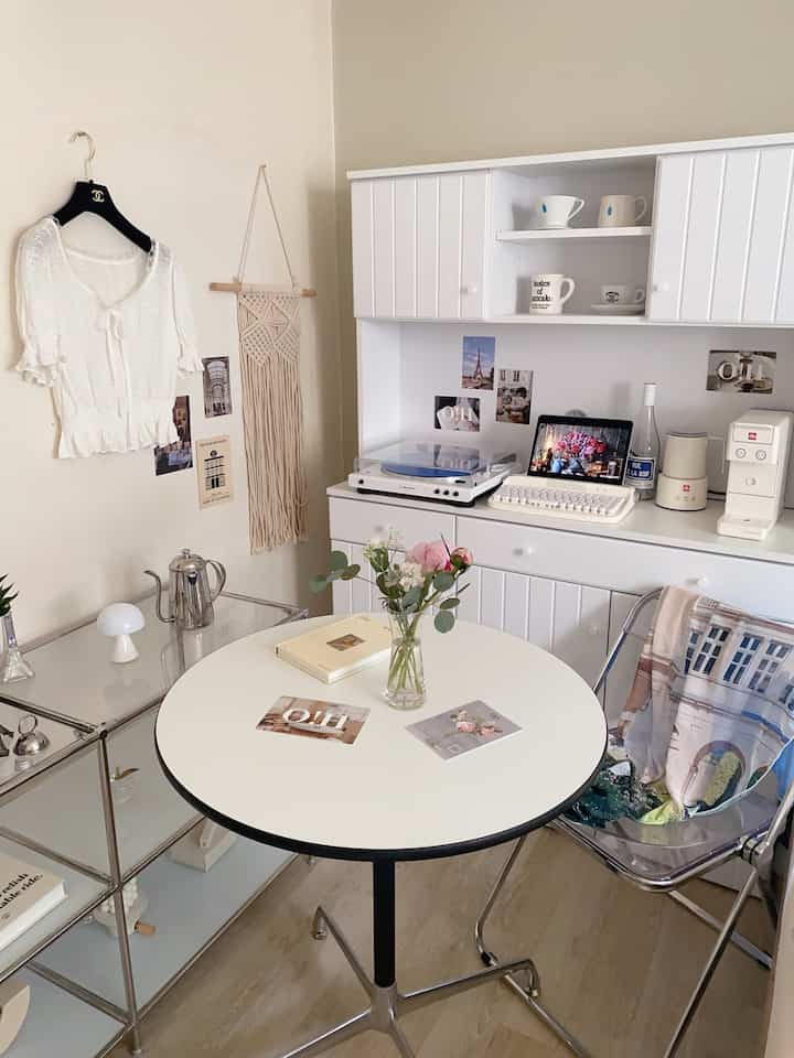 Bright white toned kitchen and home cafe space featuring round dining table, transparent chair, and cozy flower decor