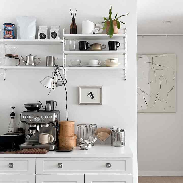 A clean and modern home cafe kitchen in white and natural tones, featuring shelves and a coffee machine