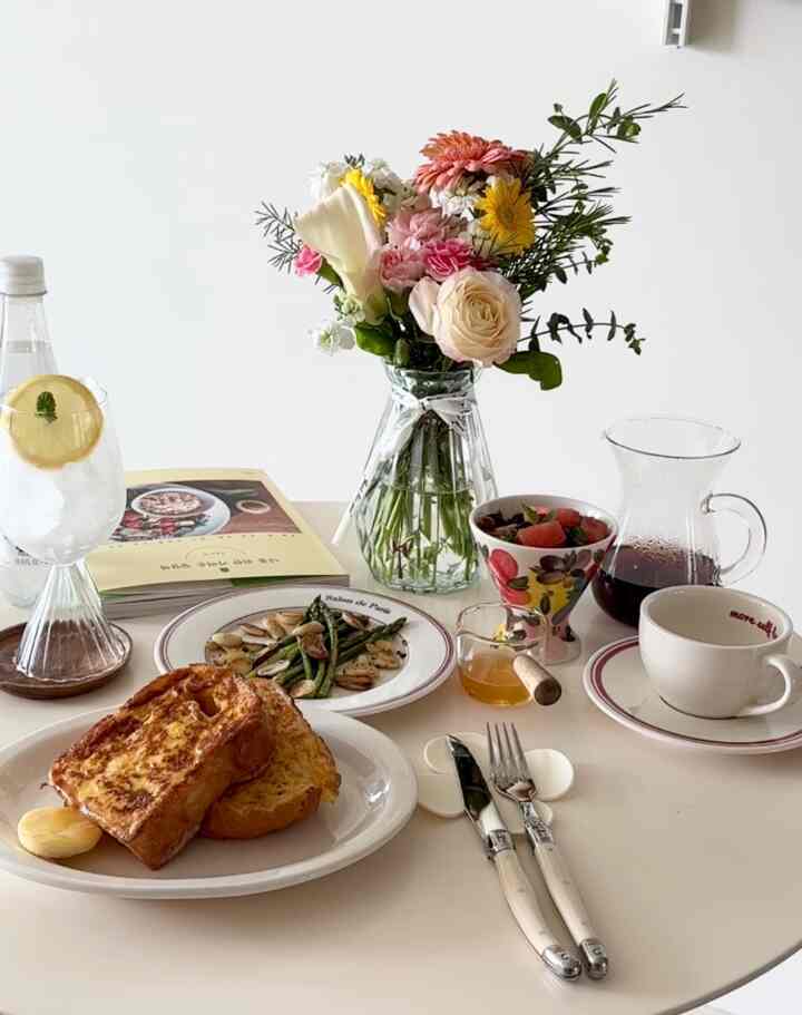 White-toned home cafe style dining table featuring fresh flower vase, French toast, and asparagus dish in a cozy setting