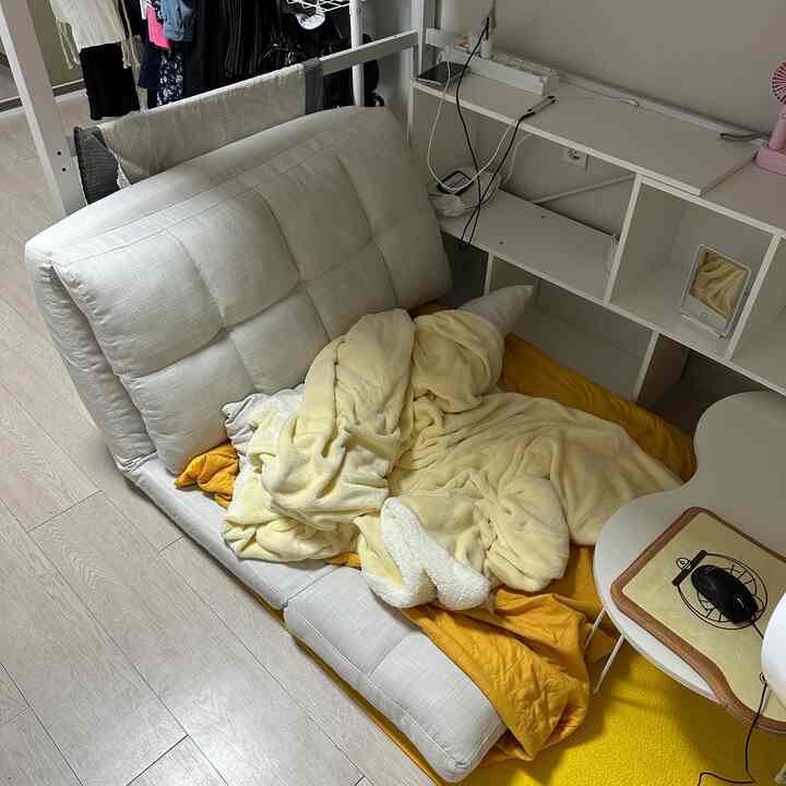 白と黄色のトーンのワンルーム寝室、折りたたみ式ソファベッドとラグが配置された落ち着いた空間