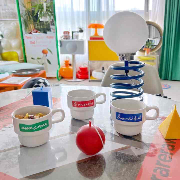 Bright kitchen space with white and yellow tones, featuring cute lettering mugs and a unique spring lamp on a glass table, creating a cheerful atmosphere