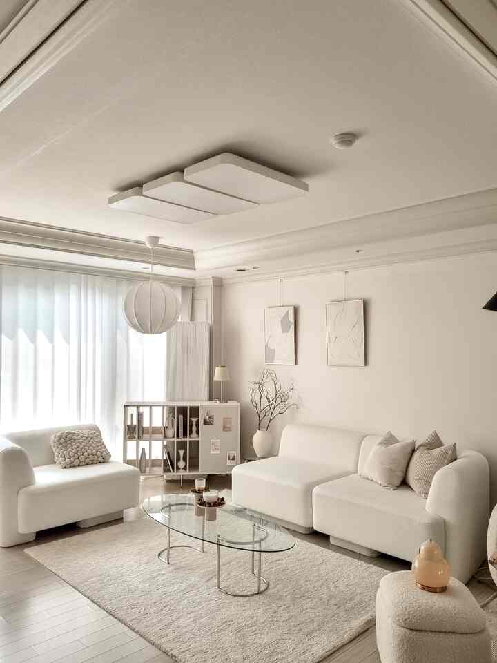 White-toned living room featuring natural modern style sofas, transparent coffee table, and minimalist storage cabinet creating a harmonious space