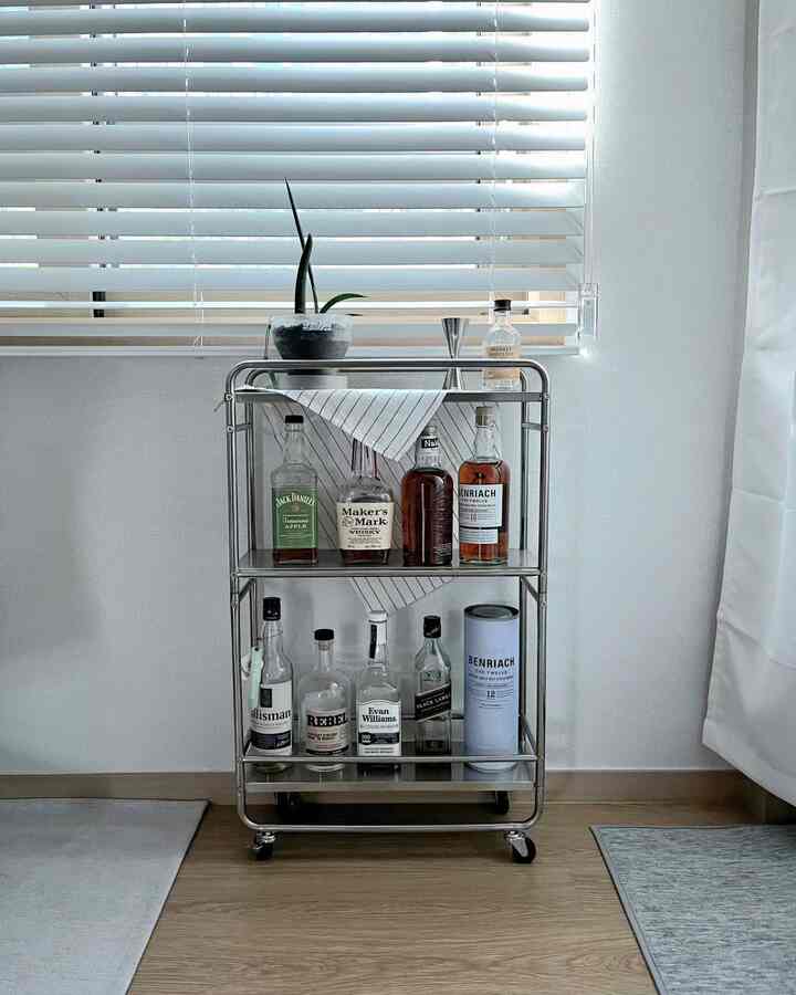 白と木目調のリビングに、ステンレス製の移動式トロリーにウイスキーボトルが並んだミニマルなインテリア