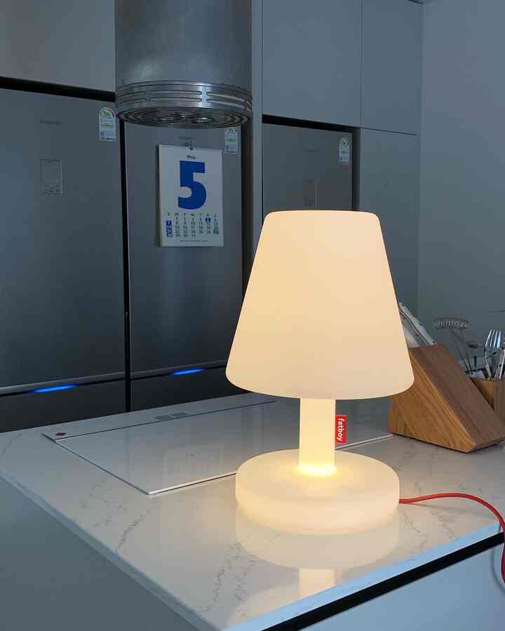 White and silver toned kitchen featuring a glowing table lamp center-right and wooden utensil holder, presenting a clean modern interior
