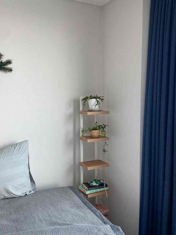 落ち着いたブルートーンとナチュラルウッドのコーナー棚が配置された居心地の良い寝室