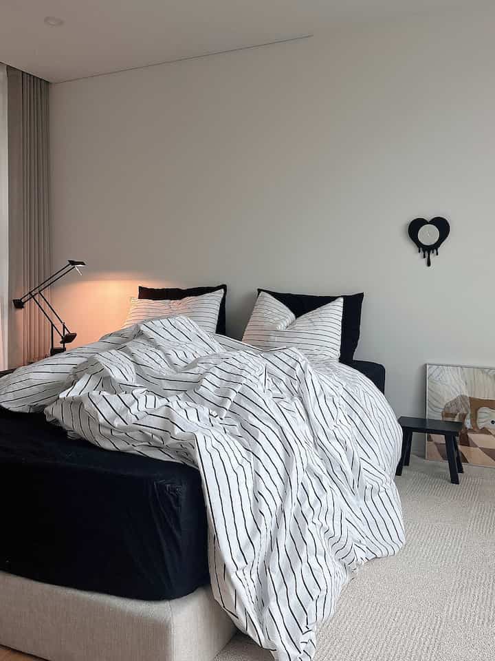 白い壁と黒いベッドフレーム、ストライプの寝具が調和したモダンな寝室のインテリア