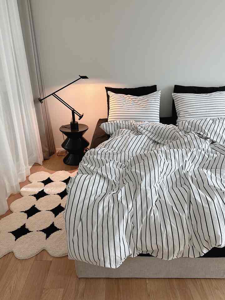 Modern style bedroom featuring black and white striped bedding, black nightstand with table lamp, creating a calm atmosphere