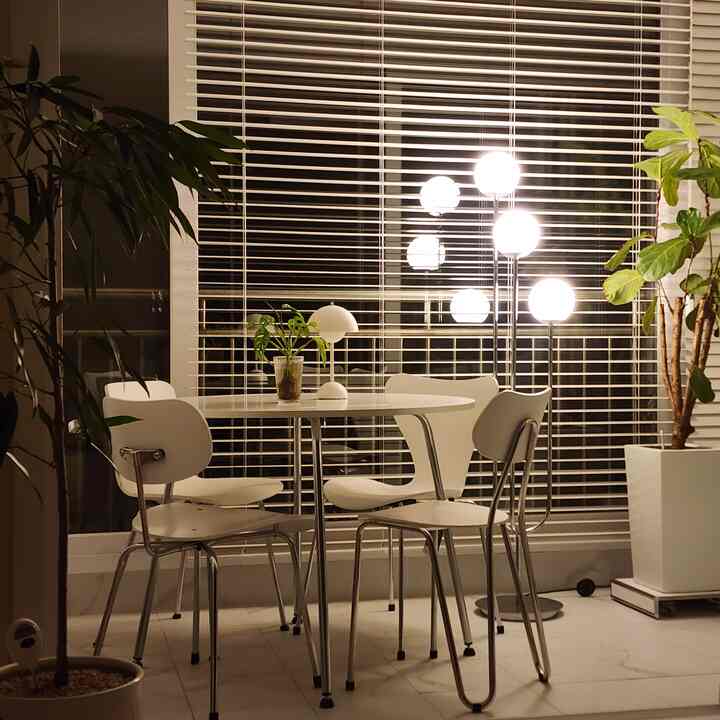 A modern dining room in white and natural tones featuring a round table, chairs, plants, and soft ambient lighting