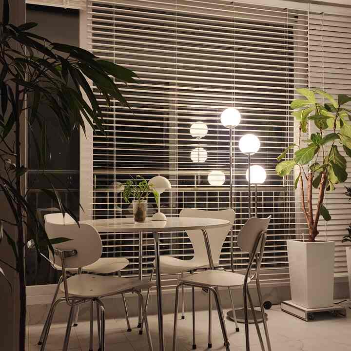 Natural-toned veranda home cafe featuring white round table and chairs with green plants and warm floor lamps creating a cozy atmosphere