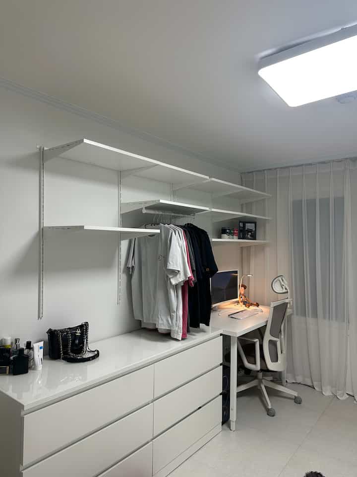 Bright and clean white-toned walk-in closet featuring drawers, shelves, and a computer desk creating efficient storage and remote work setup