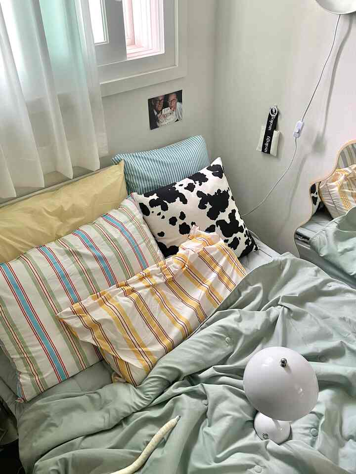 明るいベージュとブルーのトーンの寝室、様々な模様のクッションと淡いミント色の寝具が配置された落ち着いた空間