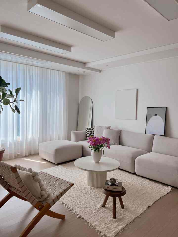 Natural white tone living room featuring a large 4-seater sofa, round coffee table, wooden stool, and bright curtains for a cozy atmosphere