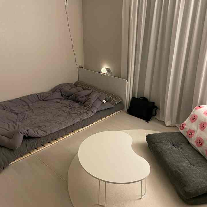 Ivory and gray toned studio apartment featuring floor mattress and modern kidney-shaped table with a clean and cozy bedroom atmosphere