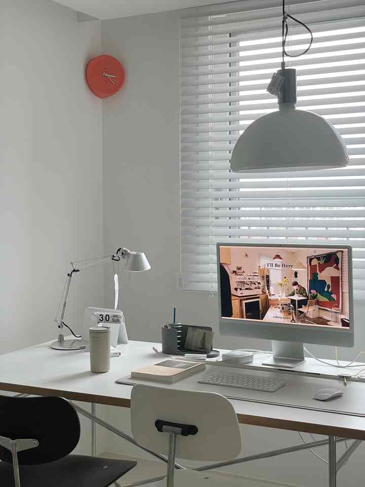 White-toned home office space featuring a wide desk with an iMac computer and a desk lamp arranged in a clean workspace