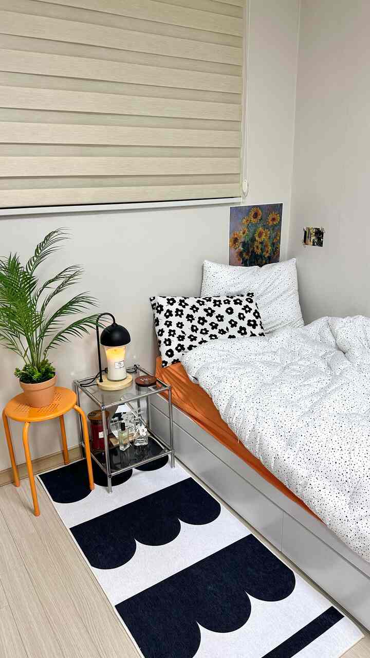 Orange-toned studio bedroom featuring white dotted bedding, an orange stool, and a plant creating a cozy atmosphere