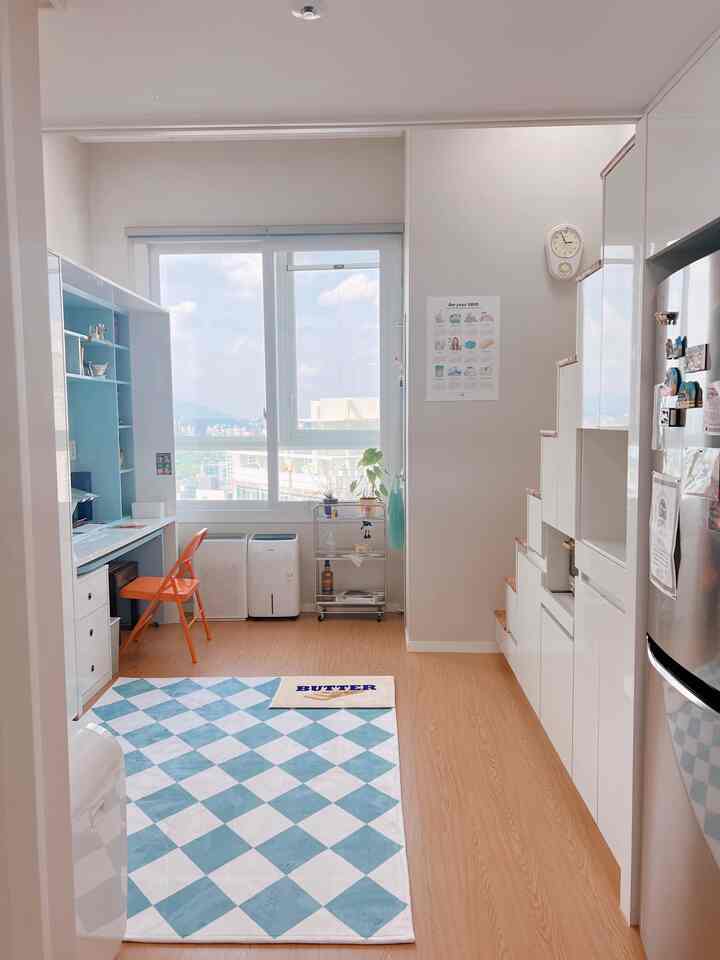 Sky blue and white tone loft kitchen space featuring a pastel built-in desk and an orange folding chair in a neat interior