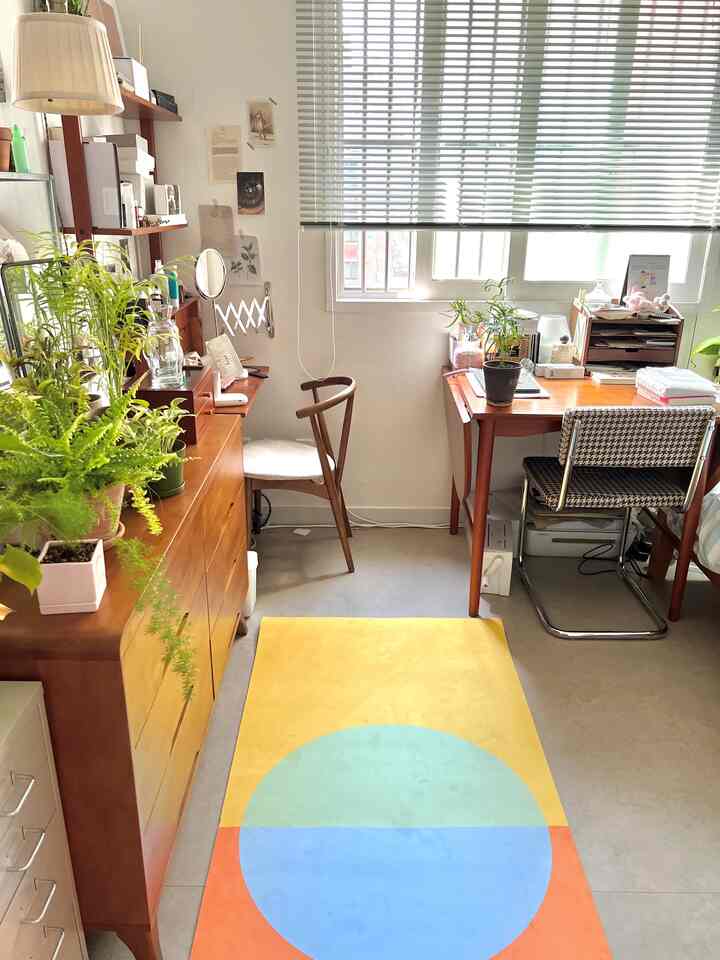 ライトブラウンの木製家具と緑の植物が配置された、狭いコンパクトなワンルームのホームオフィス空間