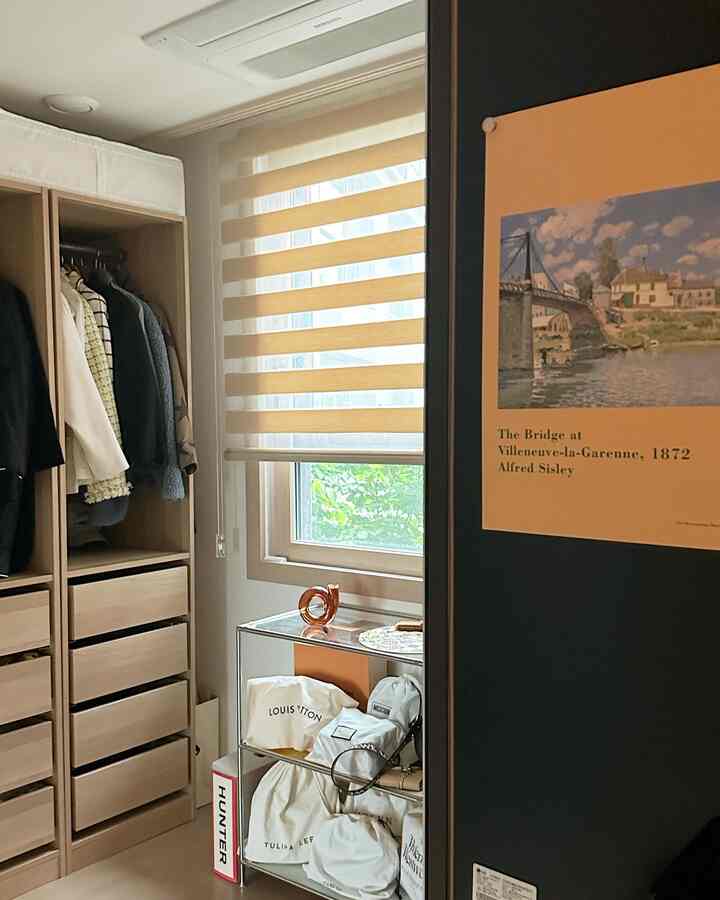 Walk-in closet with light wood tones and beige blinds, featuring neatly organized storage with a natural and calm atmosphere