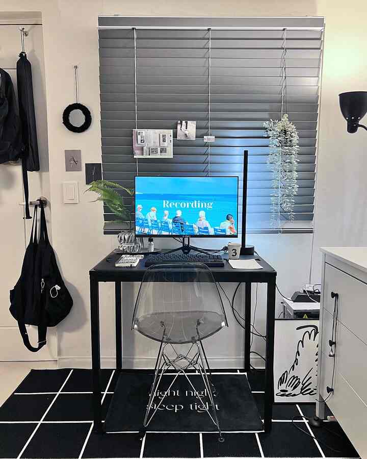 Modern studio home office in black and gray tones featuring a black desk and transparent chair with sleek decor