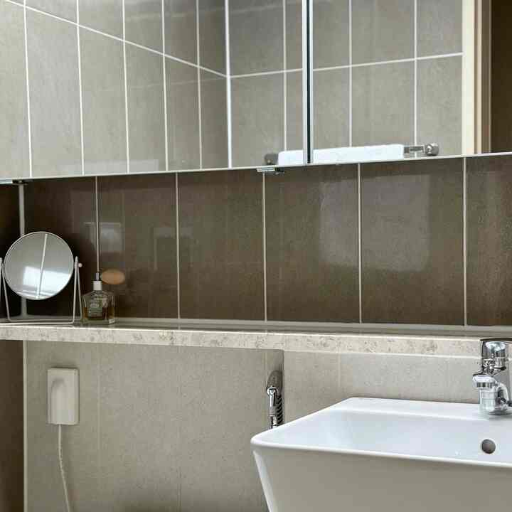 グレーのタイル壁と白い洗面台が配されたミニマルなパウダールームのバスルーム